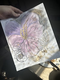 a hand holding a piece of paper with a pink flower on it