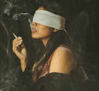 a woman smoking a cigarette with a blindfold on her face